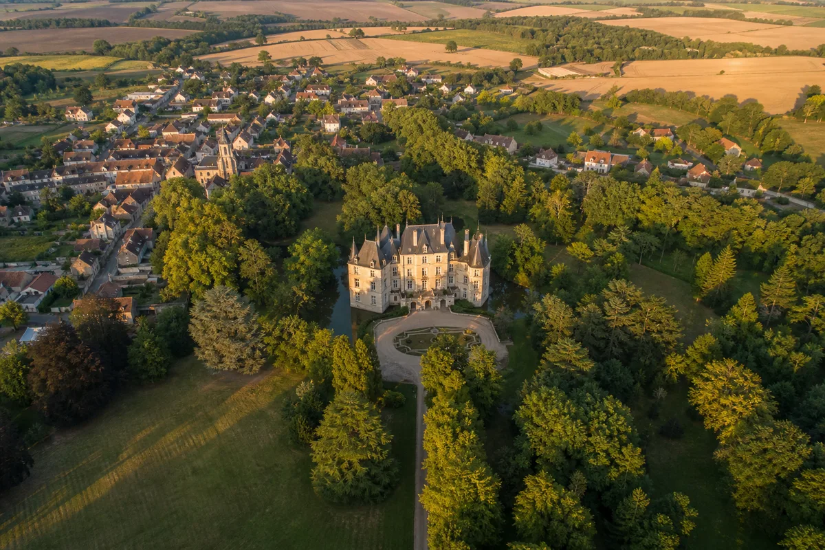 Vue aérienne d&rsquo;un château et de son parc entourés de maisons de village et de champs, campagne française en été