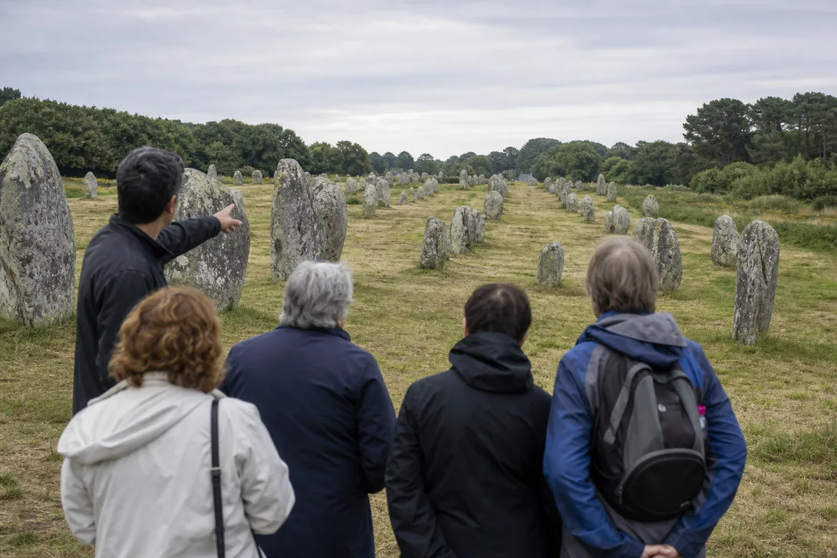 Guide commentant un site mégalithique breton devant un petit groupe de visiteurs attentifs sous une lumière naturelle
